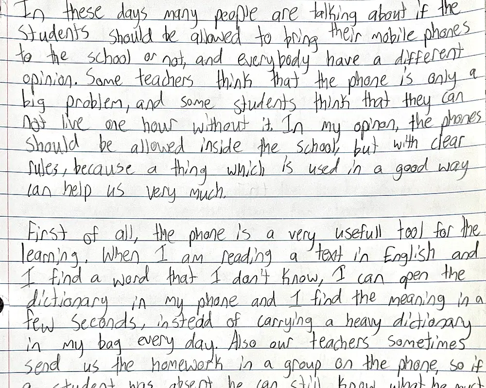 A page of lined paper filled with a pupil's handwriting in pencil: an argumentative essay about whether students should be allowed to bring mobile phones to school.